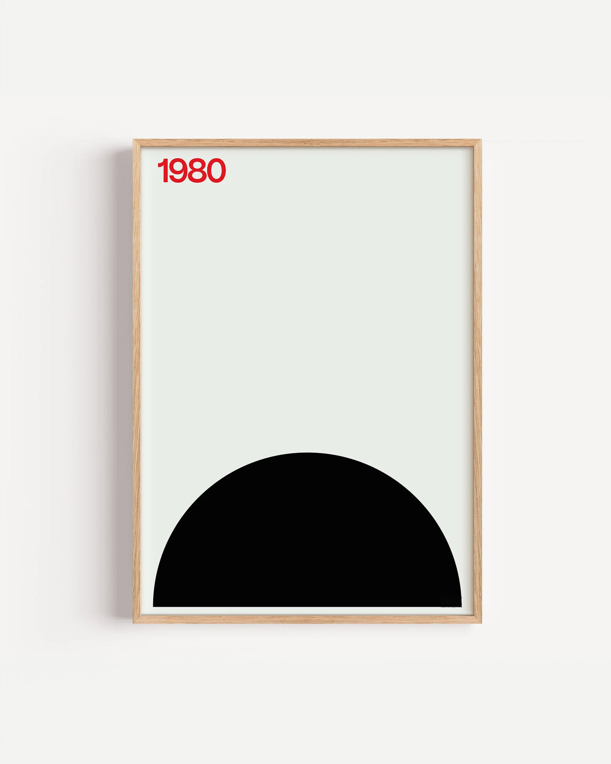 Poster 1980 di DDA in cornice rovere su parete bianca: un semicerchio nero in basso su fondo chiaro e un 1980 rosso.