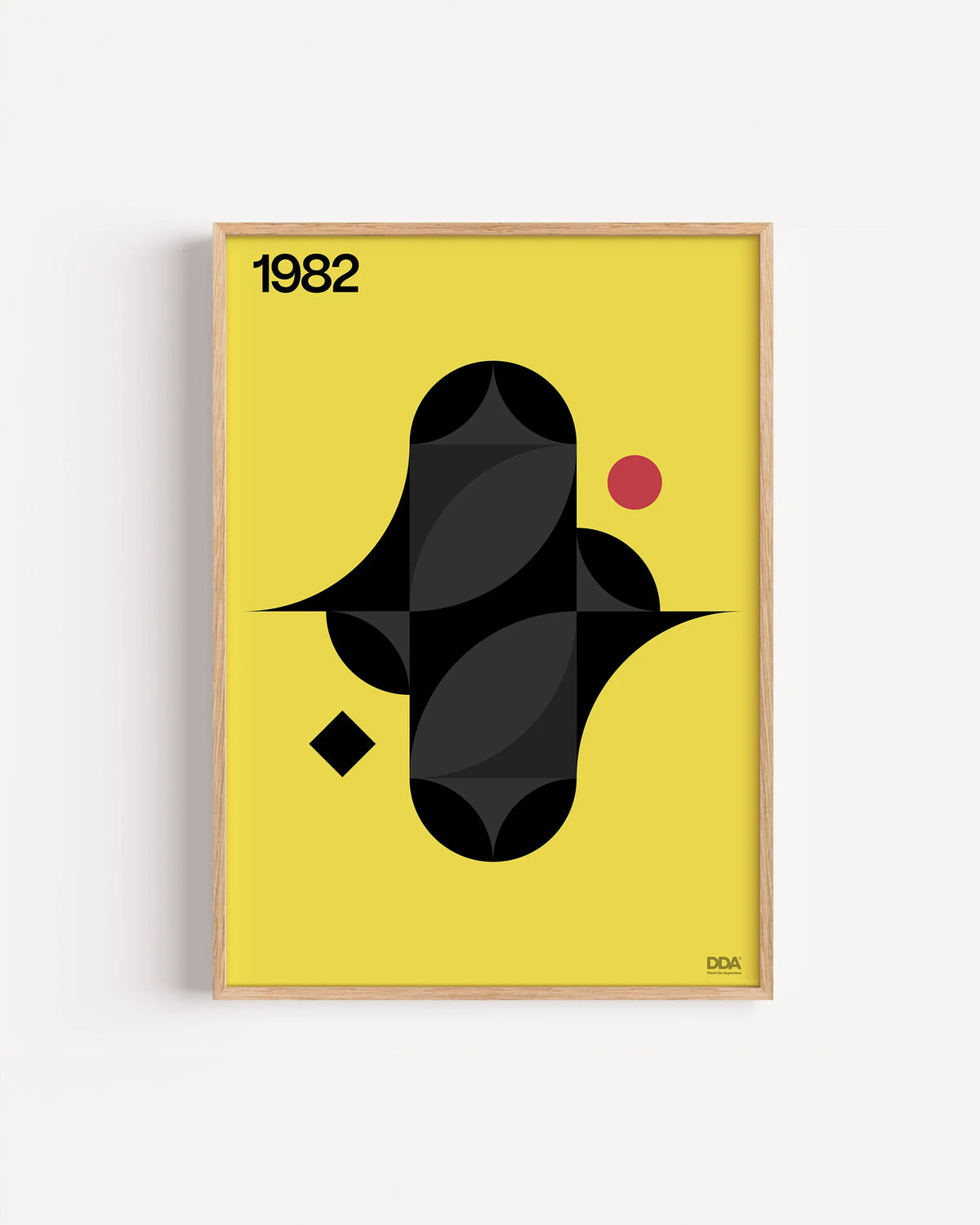 Poster 1982 di DDA in cornice rovere su parete bianca: una figura nera a forma di stella con riflessi grigi, un rombo e un pallino rosso su fondo giallo.