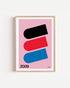 Poster 2009 di DDA in cornice rovere su parete bianca: tre capsule inclinate, nera, rossa e blu, su fondo rosa.