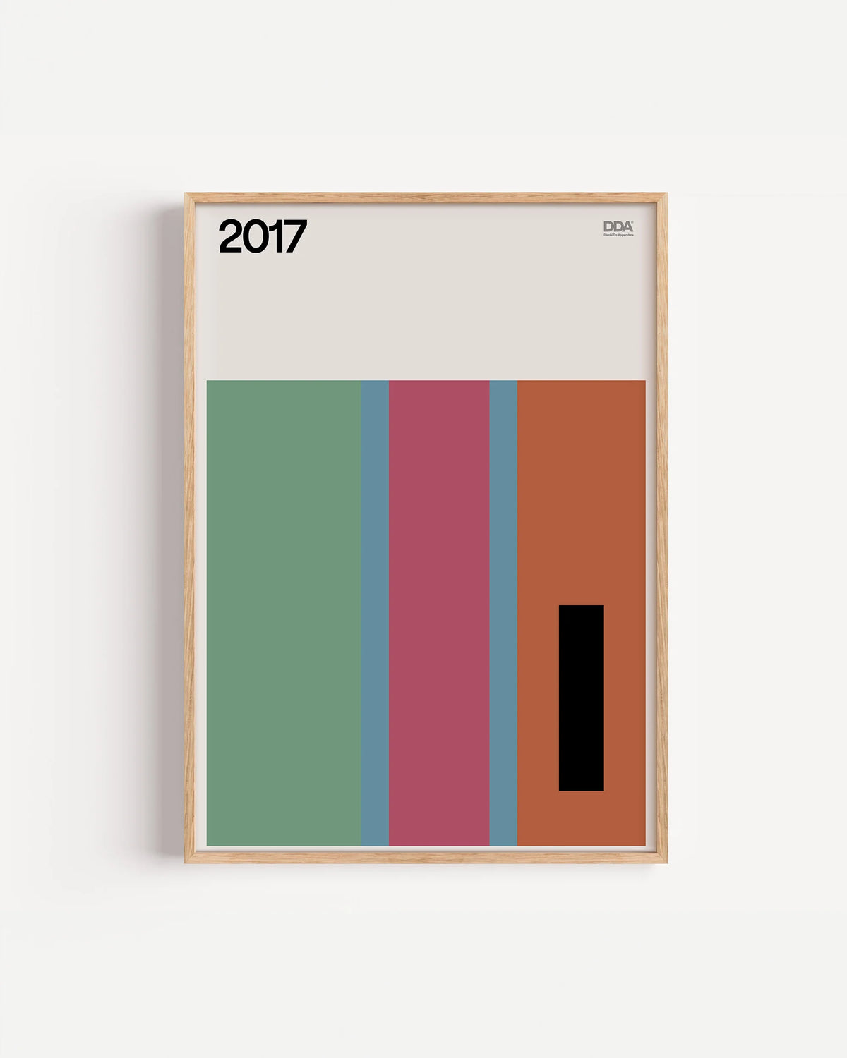 Poster 2017 di DDA in cornice rovere su parete bianca: tre fasce verticali verde, rosa e arancio con un rettangolo nero, su fondo chiaro.